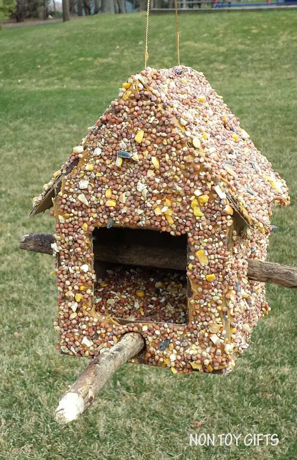 This DIY bird feeder is a fun spring or summer craft to make with kids. You only need a cardboard box, a hot glue gun, two sticks, peanut butter and seeds. | at Non Toy Gifts
